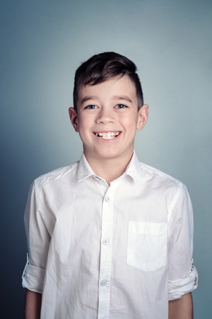 cute boy in a white shirt is standing, looking at the camera and smiling. Vertical compositionの写真素材