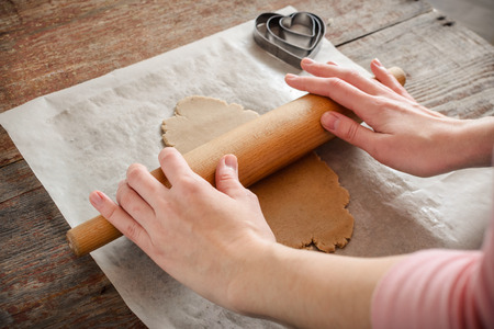 a young woman is cooking homemade ginger biscuits. Rolls the dough on a wooden table with a rolling pinの写真素材