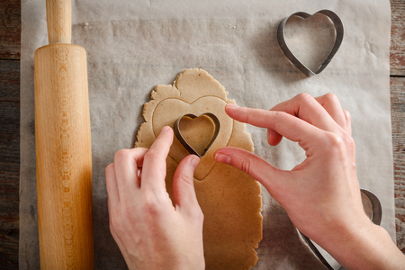 a young woman is cooking homemade ginger biscuits. Cut out heart-shaped doughの写真素材