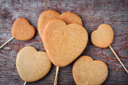 Ginger cookies on a stick in the form of hearts are piled in a heap on a wooden table. Top view, flat layの写真素材