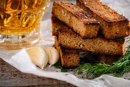 Rye croutons with dill and garlic as a snack and light beer in a glass mug on a wooden tableの写真素材