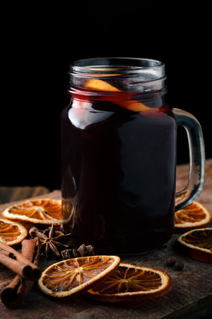 Mulled wine in a glass mug with oranges, cinnamon sticks and anise on a wooden table.の写真素材