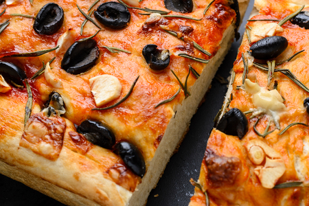Traditional Italian vegetarian focaccia of homemade bread with olives, rosemary and garlic on a close-up background.の写真素材