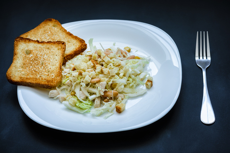 Salad of cabbage and beans and fried croutons on a white plate on a black backgroundの写真素材
