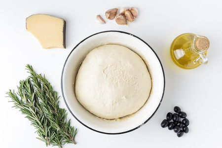 ingredients for homemade Italian focaccia top view in a flat style. Dough in a white bowl, rosemary, garlic, cheese, olives and olive oil on a white background.の写真素材