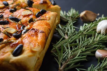homemade Italian focaccia with rosemary, olives and garlic on a dark background, close-upの写真素材