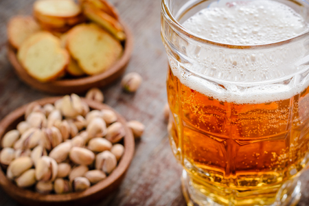 A mug of light beer with foam and pistachios on a wooden table in the backlightの写真素材