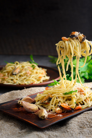 Italian pasta in a creamy sauce with seafood, shrimps and mussels on a fork on a dark wooden backgroundの写真素材