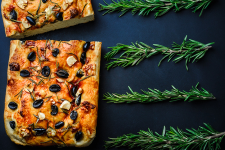 Traditional Italian vegetarian focaccia of homemade bread with olives, rosemary and garlic on a close-up background.の写真素材