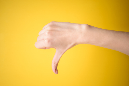 Thumb down female hand sign isolated on yellow backgroundの写真素材