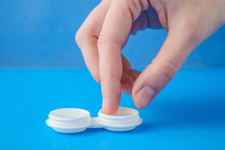 Close up view of female hands taking lens out of container on blue backgroundの写真素材