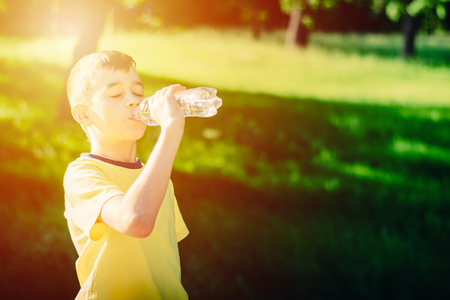 Little boy drinking  water from the plastic bottle in summer park, toned photoの写真素材
