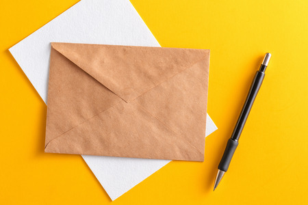Blank white card with kraft brown paper envelope and pencil on yellow background template mock upの写真素材