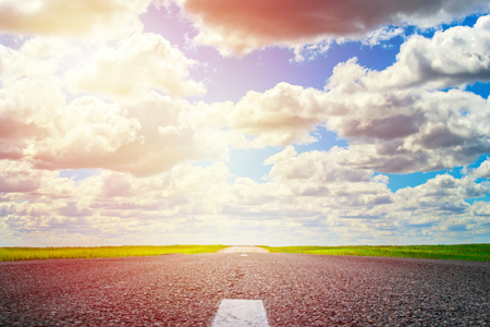 asphalt road through the green field and clouds on blue sky in summer dayの写真素材
