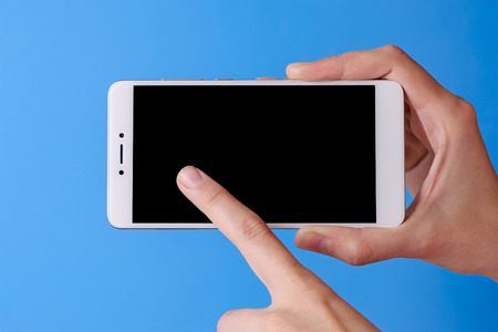 woman's finger touching on phone mobile with isolated display. hands and smartphone on blue backgroundの写真素材