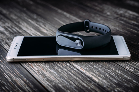 Black fitness tracker on white smartphone on wooden table. Closeup, selective focusの写真素材