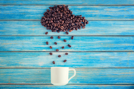 Coffee beans in shape of cloud pouring rain in white cup on blue background. Concept art photoの写真素材