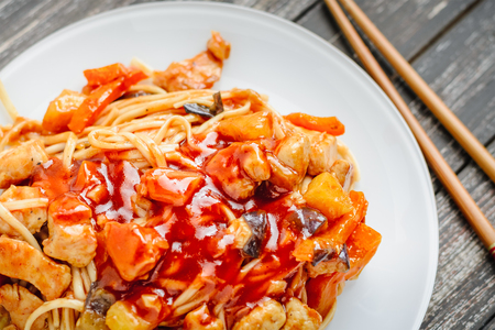Wok. Udon stir fry noodles with chicken and vegetables in a white plate on black wooden background. With chopsticks and sauceの写真素材