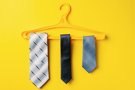 three men's ties are hanging on hanger on yellow backgroundの写真素材