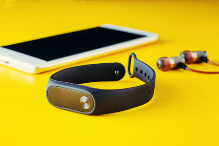 Fitness tracker, headphones and smartphone on yellow background close-up