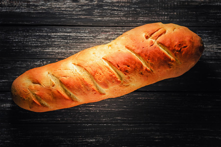 Fresh homemade loaf of bread on wooden background, top view, dark key