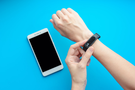 close up sport girl using fitness tracker on hand and smartphone on blue background close upの写真素材