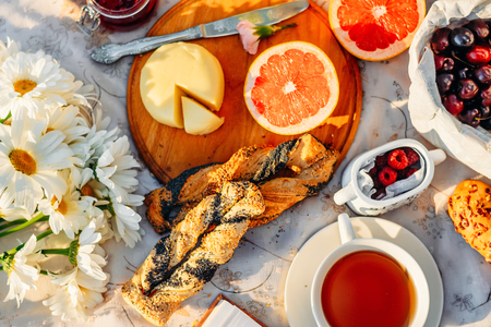 outdoors park food. Fruits, croissants, tea and flowers on tablecloth in summer sunlight. Picnic conceptの写真素材