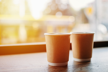 two paper cups of coffee near the window of cafeの写真素材