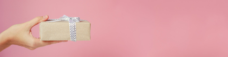 Woman hand holds gift box on pink background, banner with copy space