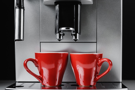 Modern coffee machine and two red cups at black background, close upの写真素材