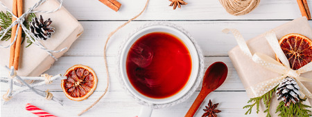 Christmas decorations with gift boxes, pine cones and cup of tea on white wooden background, long bannerの写真素材