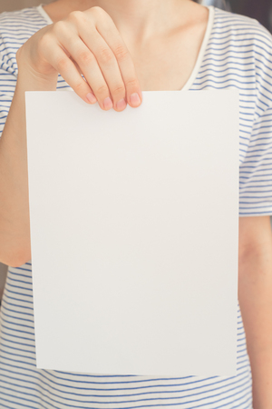 Caucasian woman in striped t-shirt hold white blank paper sheet in handの写真素材