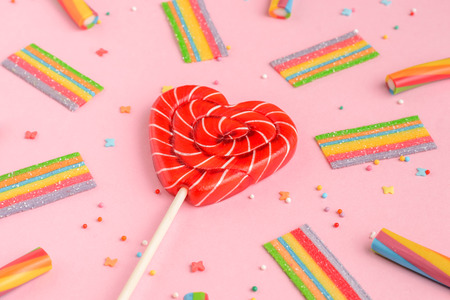 Red lollipop in shape of heart and colorful sweets on pink background, flat layの写真素材