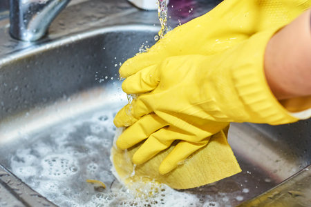 Hands in yellow gloves cleaning sink in kitchenの写真素材