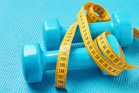 Fitness concept. Dumbbells and measuring tape on blue background, close upの写真素材