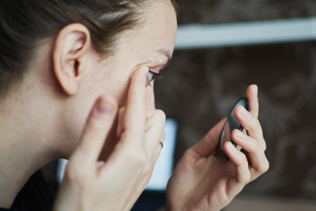 woman applying cream and looks at hand mirrorの写真素材