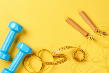 Fitness concept with blue dumbbells, measuring tape and jump rope on yellow background. top view with copy spaceの写真素材