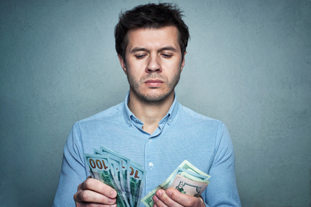 Portrait of caucasian man in shirt counting money on gray wall background. Business and financial conceptの写真素材