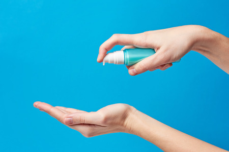 Woman hand using wash hand hygiene gel pump dispenser on blue background, female skin careの写真素材