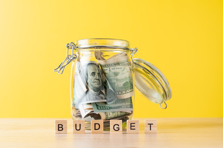 glass jar filled with dollars and word budget made of wooden blocks on yellow backgroundの写真素材