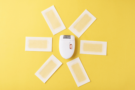 Epilator and wax strips on yellow background. Set for depilation, bodycare conceptの写真素材