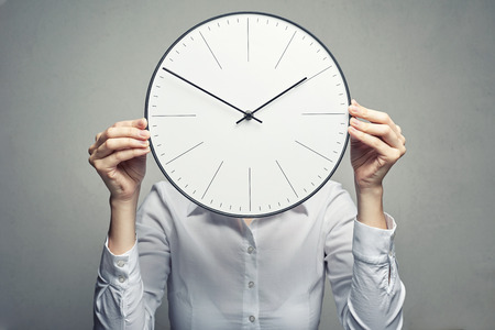 business woman in white blouse covering her face with clock