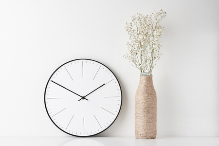 Front view desk with round wall clock and flower in bottle vase on white background. Home office minimal workspace deskの写真素材
