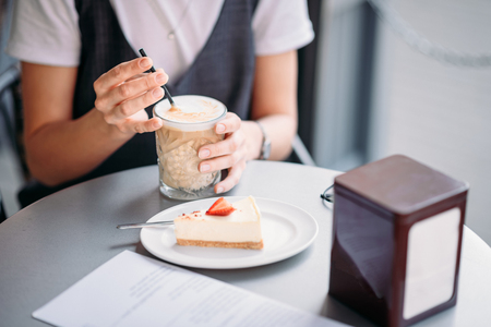 Woman drinks coffe and eat cake at the table of cafe in summer day outdoorの写真素材
