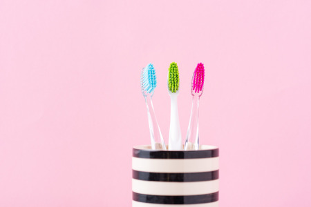 Three plastic colorful toothbrushes in glass on pink background, close up