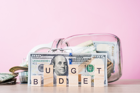 Saving money and planning budget concept. Dollar bills in glass saving bank and word budget on pink backgroundの写真素材