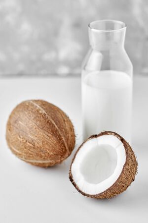 Coconut milk in glass bottle and fresh coconuts with half on gray backgroundの写真素材