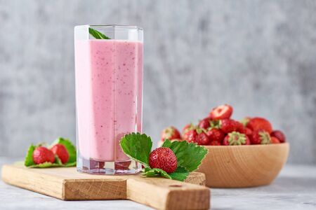 Strawberry smoothie in glass jar and fresh strawberries in wooden bowl on cutting boardの写真素材