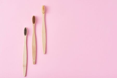 three wooden bamboo toothbrushes on pink background, top view.  Dental care concept