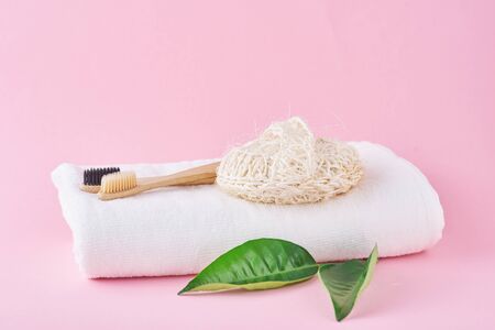 Two wooden bamboo eco friendly toothbrushes, towel and washcloth on pink background